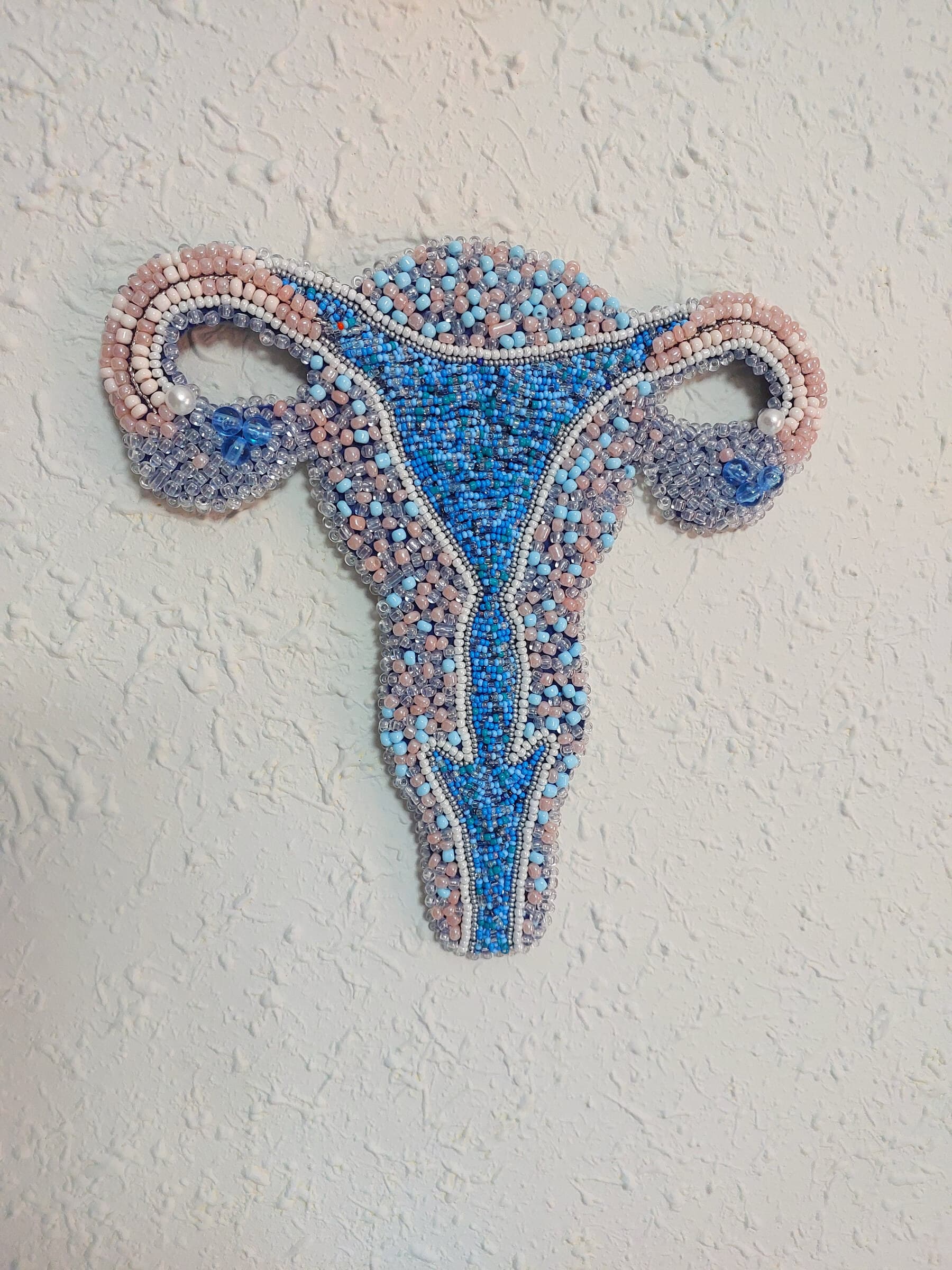 Útero bordado en abalorios azules y rosas, sobre la pared